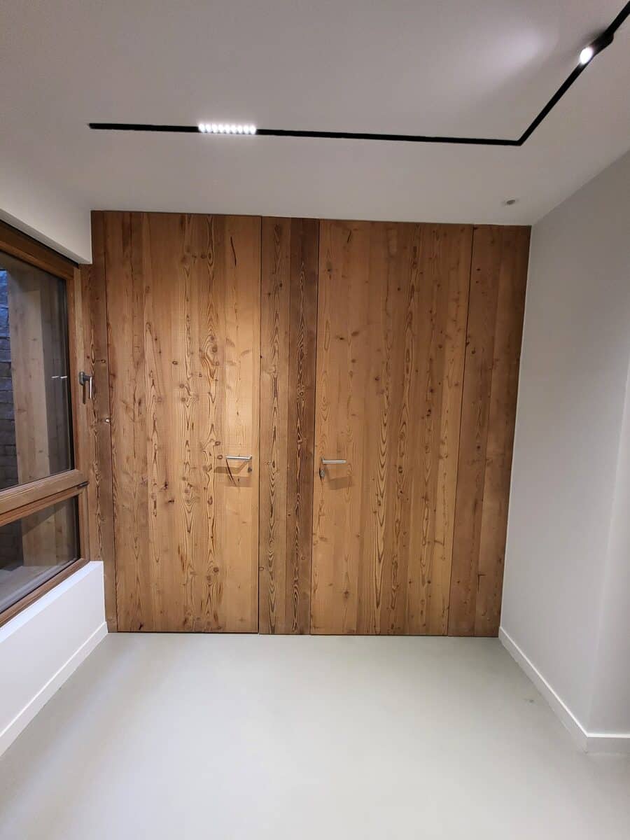 Armoires en bois rustique avec poignées métalliques, éclairage LED moderne au plafond et grande fenêtre en bois.