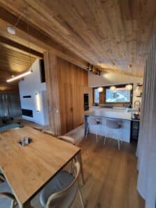 Intérieur moderne spacieux avec plafond, murs et sol en bois clair. Cuisine îlot, salle à manger bois, salon cheminée.