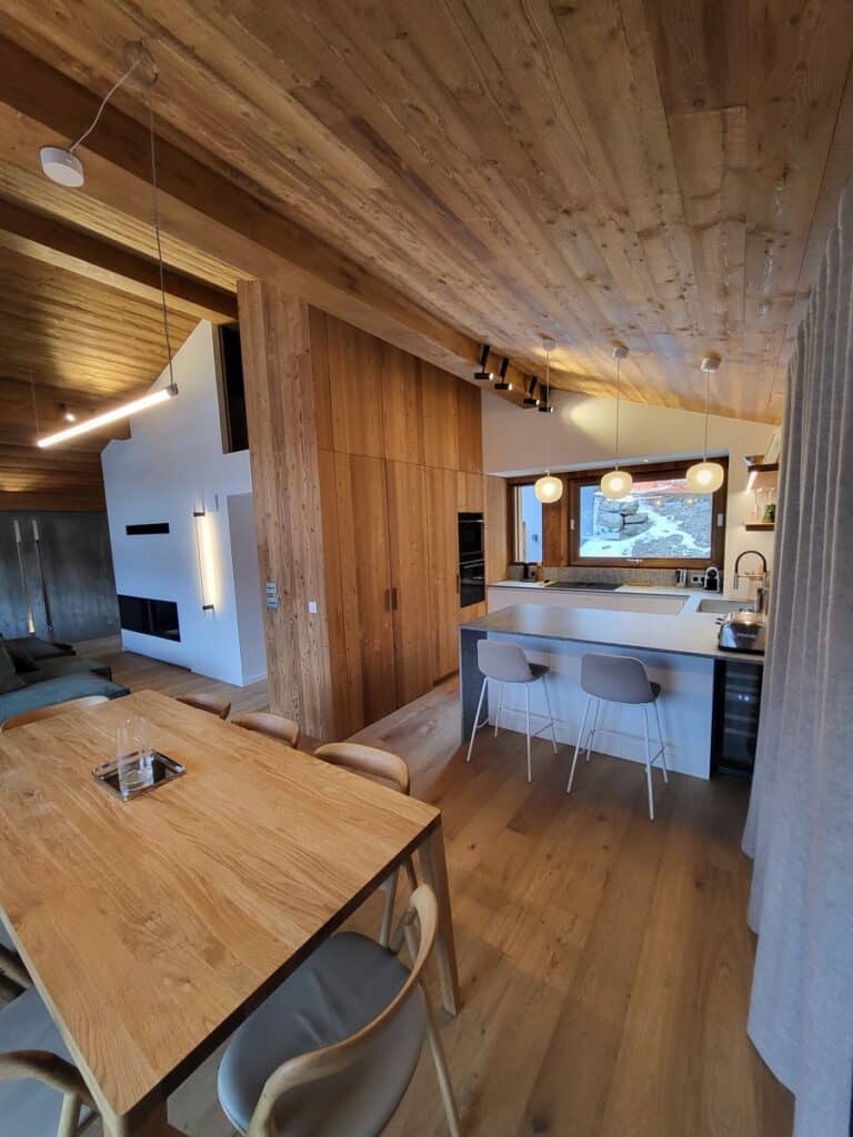 Intérieur moderne spacieux avec plafond, murs et sol en bois clair. Cuisine îlot, salle à manger bois, salon cheminée.