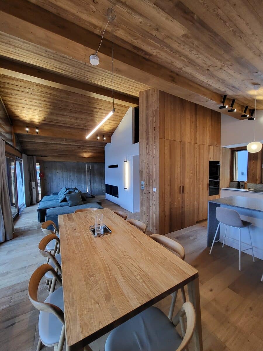 Ambiance chalet moderne en bois: salle à manger, salon avec canapé gris et cuisine ouverte. Intérieur lumineux au design épuré.