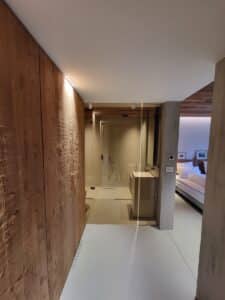 Design moderne: mur en bois, salle de bain vitrée avec douche et lavabo, menant à une chambre lumineuse avec lit. Éclairage discret.