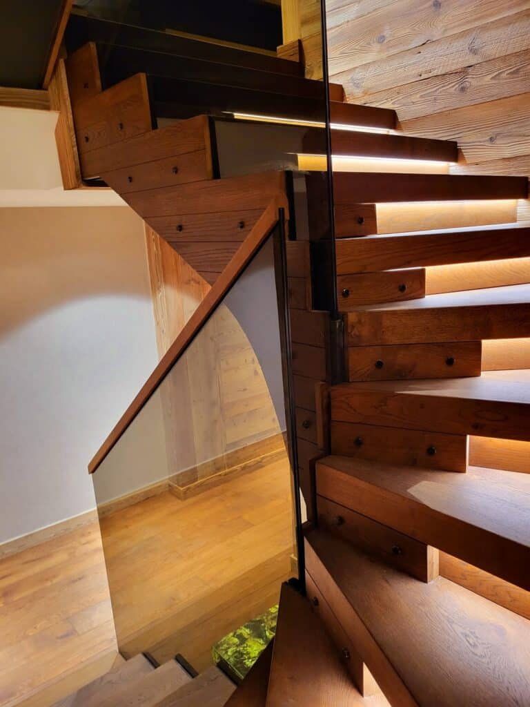 Escalier moderne en bois clair avec éclairage LED intégré sous chaque marche, rampe vitrée et mur en lattes. Ambiance chaleureuse et design.