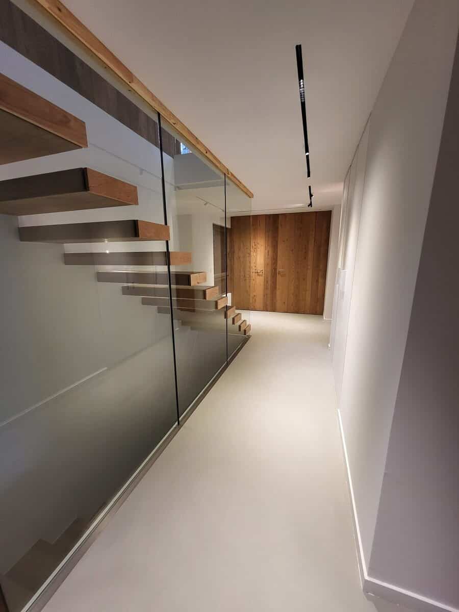 Escalier flottant en bois, rampe verre. Couloir moderne lumineux: spots au plafond, éclairage discret au sol, mur en bois au fond.