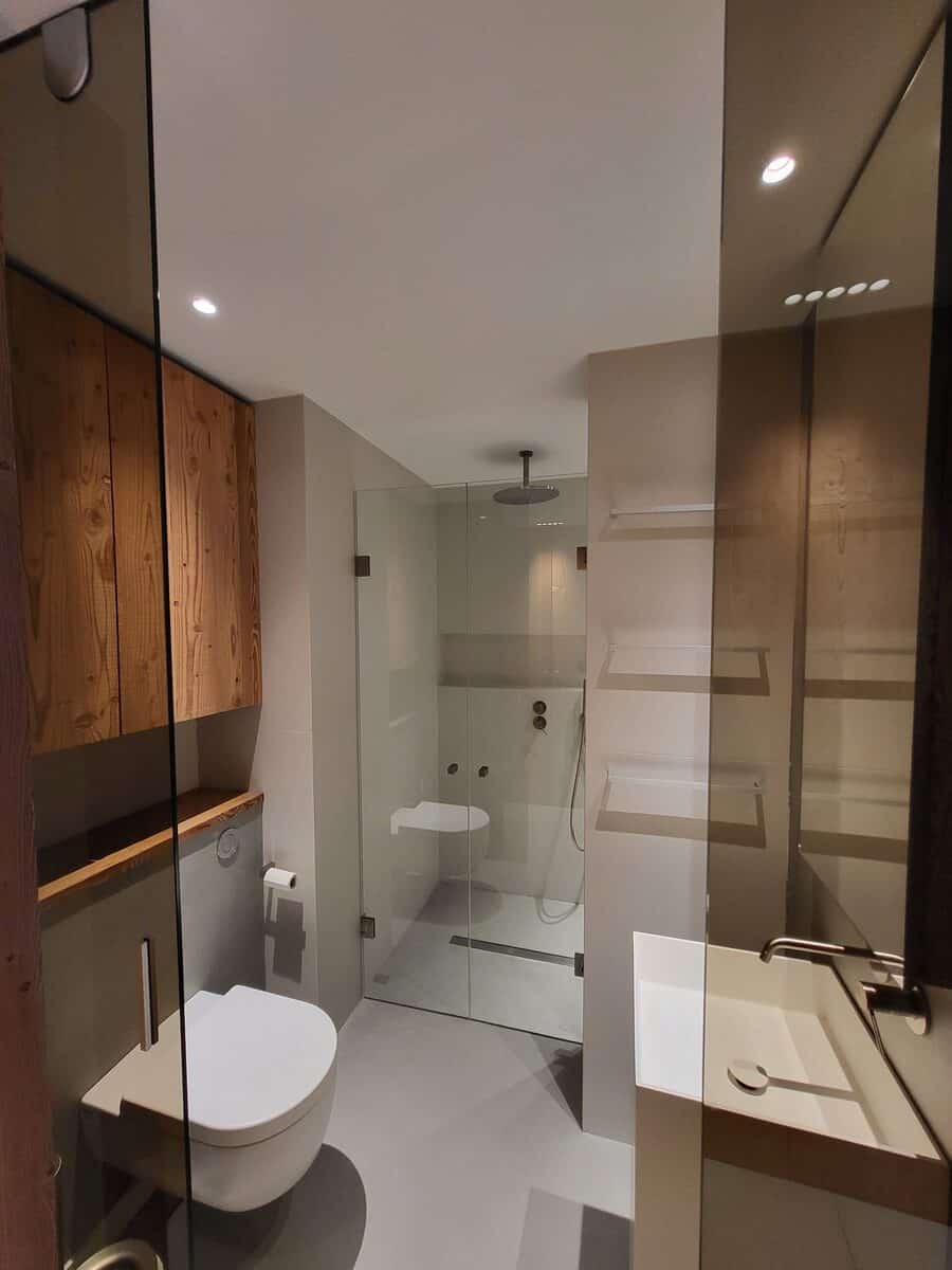 Salle de bain élégante. WC suspendu, douche à l'italienne vitrée avec siège, lavabo design, robinetterie cuivrée et mobilier en bois naturel.