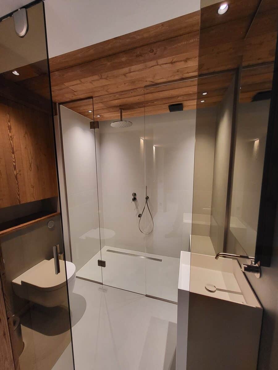 Salle de bain moderne lumineuse: douche à l'italienne vitrée, WC suspendu, lavabo design, plafond en bois texturé.