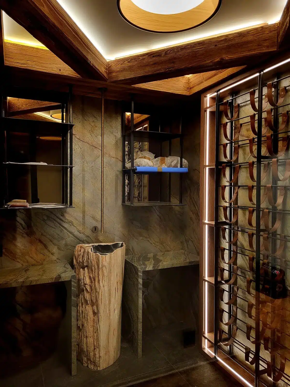 Cave à vin rustique-chic avec lavabo en bois pétrifié, murs en pierre marbrée et casiers à bouteilles en cuir.