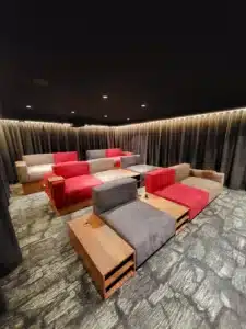 Salle de cinéma privée luxueuse avec fauteuils modulaires gris, rouges et beiges sur plusieurs rangées, éclairage d'ambiance LED.