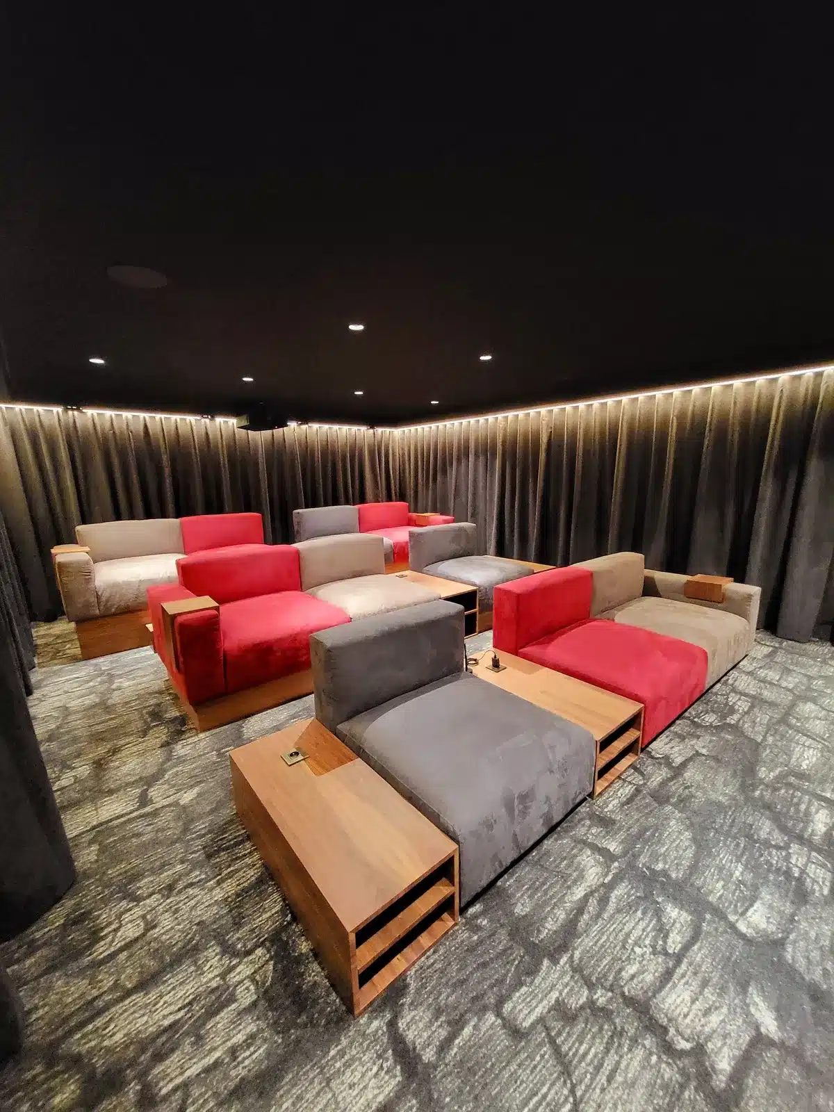 Salle de cinéma privée luxueuse avec fauteuils modulaires gris, rouges et beiges sur plusieurs rangées, éclairage d'ambiance LED.