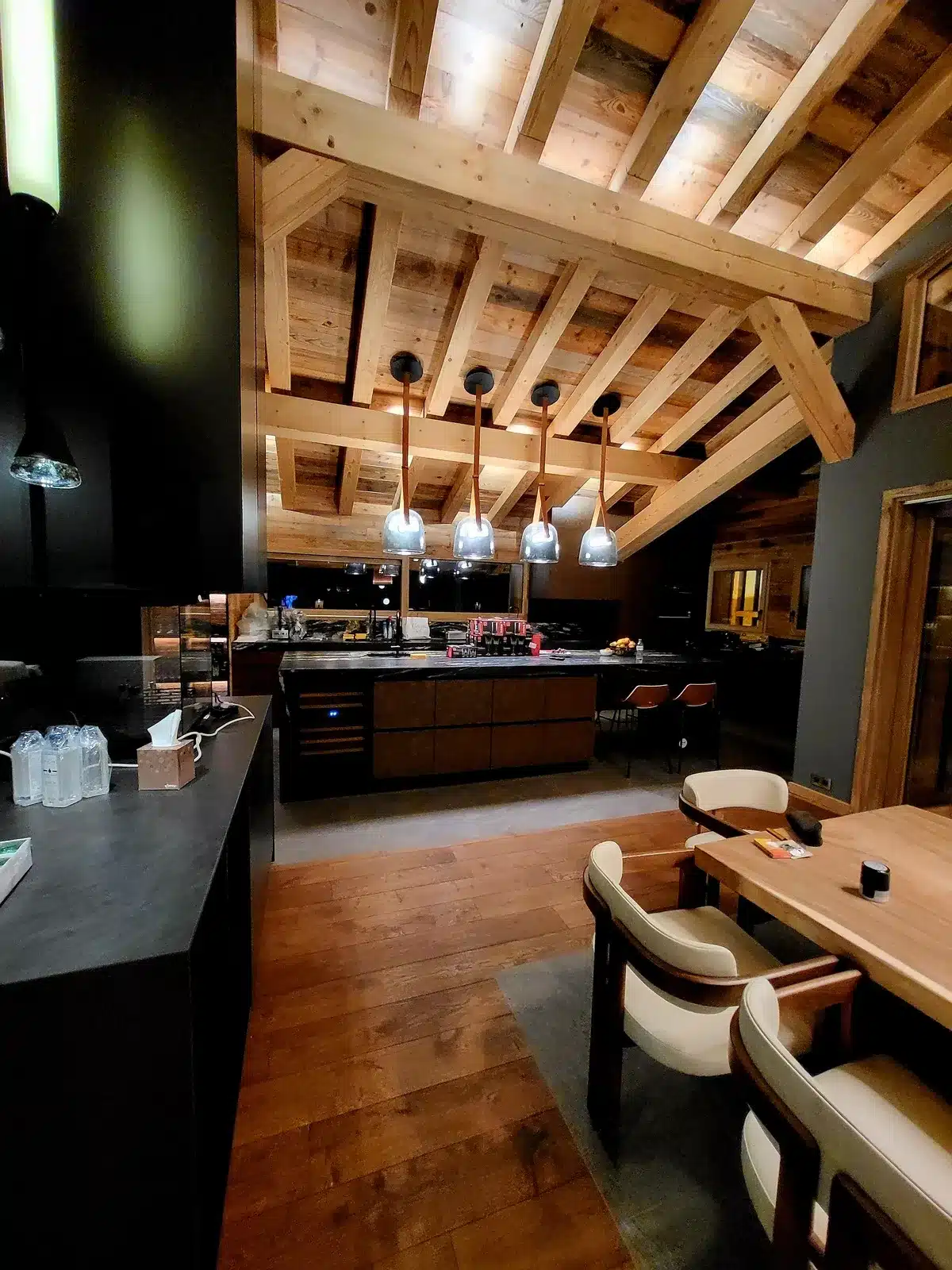 Intérieur chaleureux de cuisine de chalet moderne avec poutres apparentes en bois rustique, îlot central et luminaires suspendus design au-dessus.