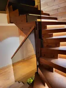 Escalier flottant moderne en bois massif foncé avec contremarches rétroéclairées par des bandes LED et une rampe en verre.