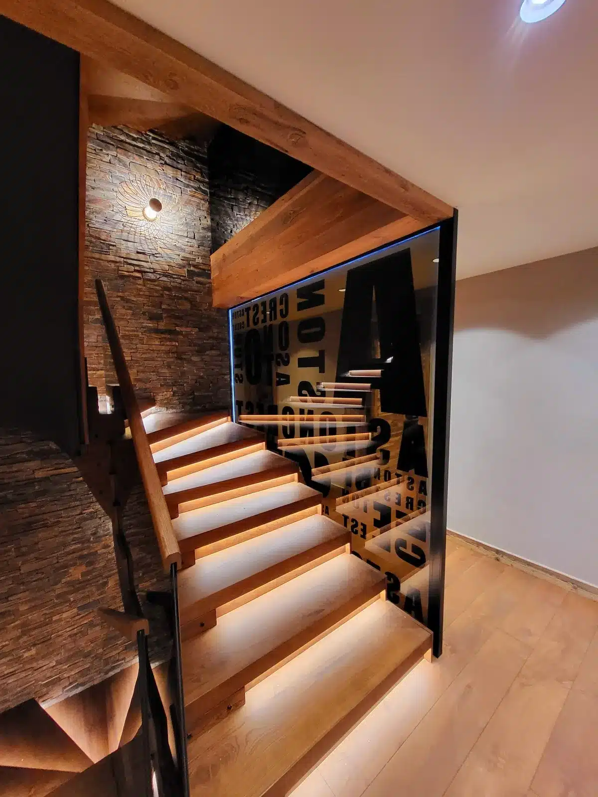 Escalier moderne bois flottant avec éclairage sous les marches et garde-corps en verre noirci sérigraphié 'CREST' et 'MOTOR'.