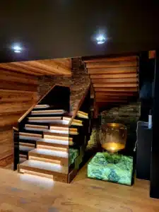 Escalier moderne avec marches éclairées par LED, rampes en verre et bois, murs en pierre et bois chaleureux, éclairage d'ambiance.