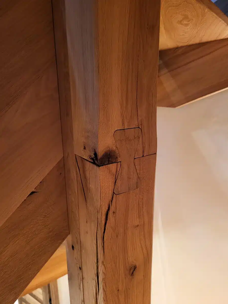 Gros plan d'un poteau de charpente en chêne rustique. L'assemblage est sécurisé par une clé papillon en bois massif.